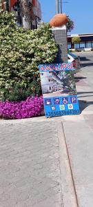 a sign sitting on the side of a sidewalk with flowers at Rooms and Apartments Analipsi in Shëngjin
