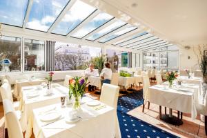 restauracja z białymi stołami, krzesłami i oknami w obiekcie Hotel von Stephan w mieście Westerland
