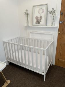 a white crib in a room with a picture on the wall at Triple Deck Cottage - 2mins from Mevagissey Harbour in Mevagissey