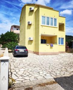 una casa gialla con una macchina parcheggiata di fronte di Sunshine Apartment a Stara Novalja Altre 5 foto
