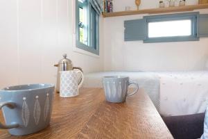 a wooden table with two cups on top of it at Dipper's Hut - Luxury Shepherds Hut with Hot Tub in Blakeney