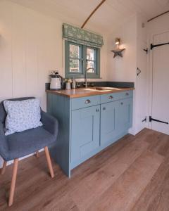a kitchen with a sink and a blue chair at Dipper's Hut - Luxury Shepherds Hut with Hot Tub in Blakeney