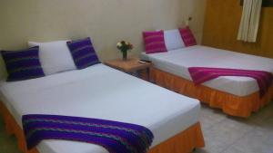 two beds in a hotel room with colorful pillows at Posada El Jardin in Ticul