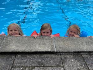 drie kinderen kijken uit over de rand van een zwembad bij Løgballe Camping & Cottages in Stouby