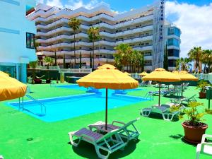 una piscina con sillas y sombrillas y un edificio en Miss Flora Olympia, en Playa de las Américas