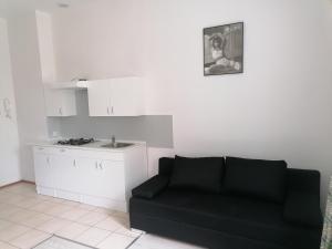a living room with a black couch and a kitchen at Przytulne Mieszkanko Centrum in Mrągowo