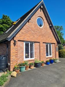 uma casa de tijolos com vasos de plantas em frente em Topsy-Turvy, Gardeners Cottage, Clungunford, Ludlow, Shropshire SY70PN em Broome