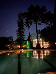 una piscina de agua por la noche con árboles y edificios en Pousada Granja Santa Barbara, en Petrópolis