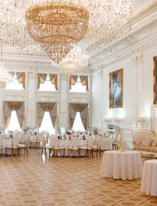 una sala banchetti con tavoli e sedie bianchi e un lampadario a braccio di Hotel Grand Aristocrate a Dubovtsy