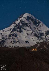 a snow covered mountain at night with a town in front at Kera Guest House in Kazbegi