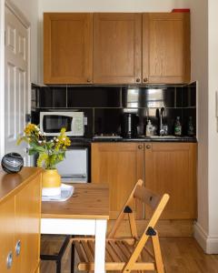 - une cuisine avec des placards en bois, une table et un four micro-ondes dans l'établissement South Kensington Courtfield Gardens studio, à Londres