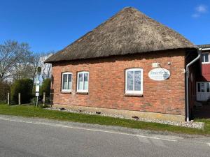 a brick building with a thatched roof on a street at Nordsee Ferienwohnung Utspann in Uelvesbüll