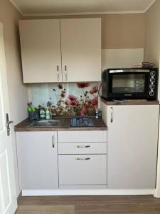 a kitchen with white cabinets and a microwave and a sink at Nordsee Ferienwohnung Utspann in Uelvesbüll