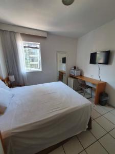 Schlafzimmer mit einem großen weißen Bett und einem Schreibtisch in der Unterkunft Praia do canto 502B in Vitória