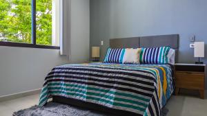 a bedroom with a bed with a striped comforter and a window at Riviera Home - New 2BR Condo w. big Pool & Jacuzzi in Playa del Carmen +22 photos