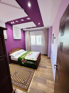 - une chambre avec un lit, des murs violets et une porte dans l'établissement Abraj Dubai Larache, à Larache