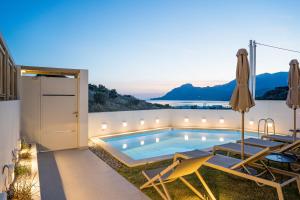 a swimming pool in a backyard with two chairs and a table at Corallia villas near the beach in Plakias