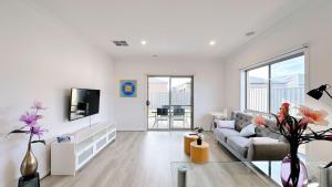 a white living room with a couch and a tv at The Grove Townhouse by GoodLive in Tarneit