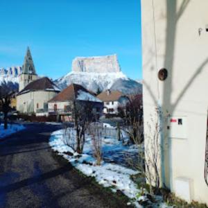 uma rua nevada com um edifício e uma montanha em La Maison Pain d'Epices em Chichilianne