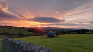 a barn in a field with the sunset in the background at Little Middop Farm Camping Pods in Gisburn