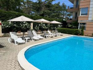 a swimming pool with chairs and umbrellas next to a building at Lovely 1-bedroom apartment with pool, 250 m to the beach in Pomorie