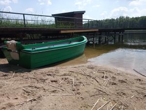a green boat sitting on the shore next to a dock at Zalesie z pomostem I in Barczewo