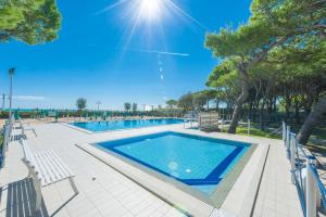 a swimming pool with chairs and trees and the sun at Park Residence Immobiliare Pacella in Lido di Jesolo