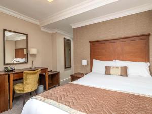 1 dormitorio con cama, escritorio y espejo en Mercure Salisbury White Hart Hotel, en Salisbury