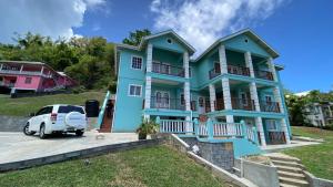 une maison bleue avec une voiture blanche garée devant elle dans l'établissement Golden Palms Apartment, à Kingstown
