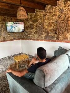un hombre sentado en un sofá viendo una tele en La Cabaña de La Nina, en Beceña