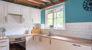 uma cozinha com armários brancos, um lavatório e uma janela em Newlands em Rusland