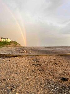 a rainbow over the beach with a house in the background at Lake District Coastal cottage in Seascale