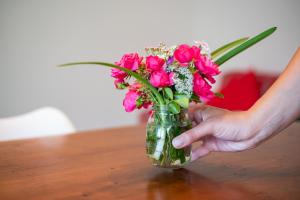 uma pessoa segurando um vaso de flores rosa sobre uma mesa em Grazioso appartamento ai piedi delle Dolomiti - SELF CHECK-IN em Cesiomaggiore