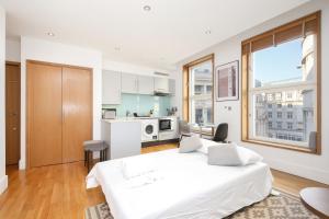 a white bedroom with a large bed and a kitchen at Imperial Piccadilly Apartments in London
