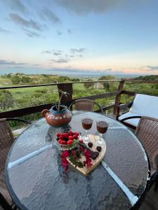 a glass table with a bowl of fruit and two glasses of wine at Chalé Mirante da Pedra in Serra de São Bento