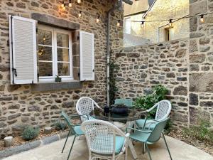 een patio met een tafel en stoelen en een stenen muur bij Petit gîte d’arrière-cour au pied du Château in Combourg