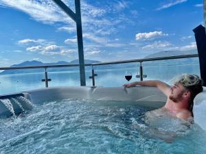 Ein Mann in einer Badewanne mit einem Glas Wein. in der Unterkunft Beach Houses with Hot Tubs in Glencoe