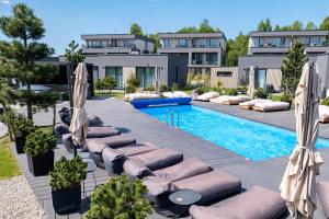 a pool with lounge chairs and umbrellas in front of a building at SMILGA & KOPA home - Mano jūra 2 Kunigiškiai - by Hello Sea homes in Palanga