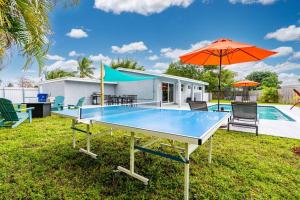 a ping pong table with an umbrella next to a pool at Spacious 5 Bedrooms with Large Pool, 12 minutes to the Ocean in Fort Lauderdale