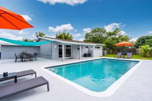 a swimming pool with an umbrella and a house at Spacious 5 Bedrooms with Large Pool, 12 minutes to the Ocean in Fort Lauderdale