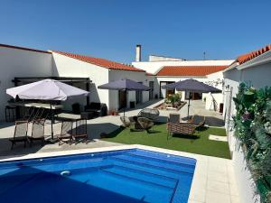 una piscina en un patio con sillas y sombrillas en Alojamiento El Miajon de los Castúos en Valdesalor