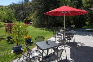 eine Gruppe von Tischen und Stühlen mit einem roten Regenschirm in der Unterkunft Parkhotel Emmaus - Casa del Sole in Ascona