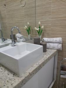 a bathroom counter with a white sink and flowers at Flats no Makambira Residence (Flats da Elena) in Porto De Galinhas
