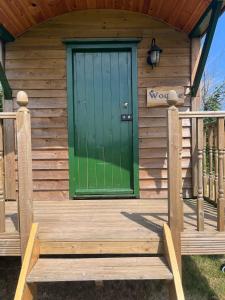 a front door of a wooden cabin with a green door at Woodie the shepherds hut - sleeps 4 in Chichester