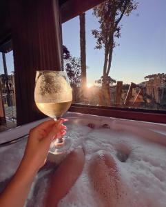 a person holding a glass of wine in a bath tub at Sunset Serrano Chalés in Urubici