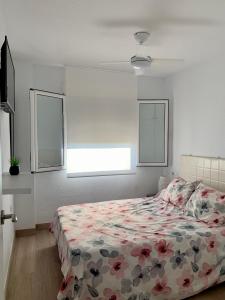 - une chambre avec un lit avec une couette à fleurs et 2 fenêtres dans l'établissement ÁTICO COPACABANA, à Playa de Gandia