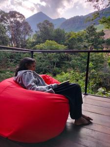 una mujer sentada en un sofá rojo en un balcón en Dumbara Breeze, en Hunnasgiriya