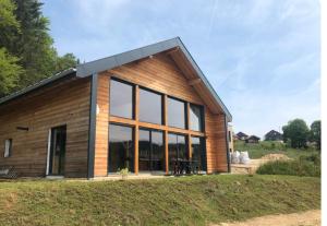 una casa in legno con ampie finestre su un campo di Chalet de vacances calme et luxueux a Lamoura Altre 2 foto