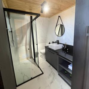 a bathroom with a glass shower and a sink at Chalé Alqualondë -Chácara Valfenda in São Joaquim