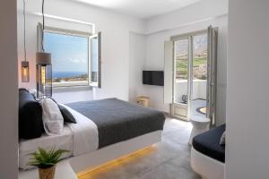 a white bedroom with a bed and two windows at Maeva Suites Santorini in Pirgos